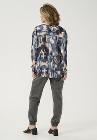 Langærmet, multicolorer skjorte med et abstrakt mønster i marineblå, lyseblå og beige, parret med grå tapered bukser og sorte hælede mules.