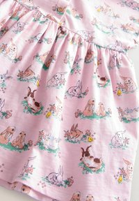Der pinke Baumwollstoff zeigt ein wiederholendes Muster aus illustrativen Kaninchen und Küken zwischen Blumen, mit einem gerafften Rockdesign und Knopfdetails.