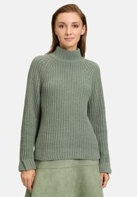Hellgrüner Strickpullover mit hohem Kragen, gerippten Bündchen und strukturiertem Muster. Der Stoff wirkt warm und gemütlich.