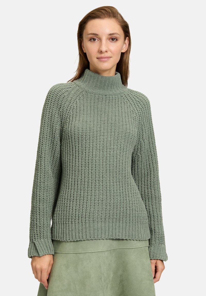 Hellgrüner Strickpullover mit hohem Kragen, gerippten Bündchen und strukturiertem Muster. Der Stoff wirkt warm und gemütlich.