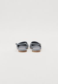 Sandales en cuir bleu avec une semelle plate, une sangle ajustable et un design minimaliste, mettant en valeur une texture lisse et un accent en bois sur le talon.