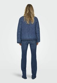 Jeans jakna s kvadratnom teksturom, plave boje, spuštenih ramena, u kombinaciji s uskim plavim trapericama, oboje s klasičnim dizajnom.