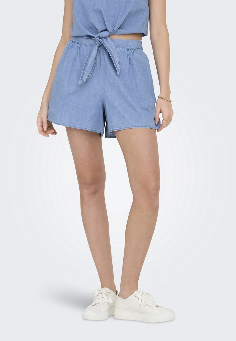 Farkkushortsit, joissa on elastinen vyötärö, vaaleansininen väri ja rento istuvuus. Yhdistetty saman sävyisen solmittavan paidan ja valkoisten tennareiden kanssa.