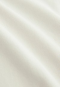 Detail hladké, krémově zbarvené tkaniny s jemnou diagonální žebrovanou strukturou a měkkými záhyby vytvářejícími jemné stíny.