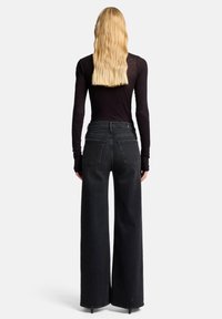 Zwarte, wijd uitlopende jeans met hoge taille, een onafgewerkte zoom en twee achterzakken, gecombineerd met een aansluitend zwart topje met lange mouwen.