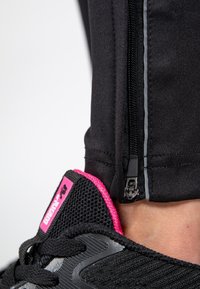 Svarta träningsbyxor med siddragkedja, grå accent, kombinerade med svarta sneakers med rosa häl och texturerat meshovansidan.