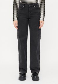 Pantaloni cargo in denim nero con vestibilità ampia, dotati di tasche laterali e una texture semplice. Abbinati a scarpe platform nere chunky.