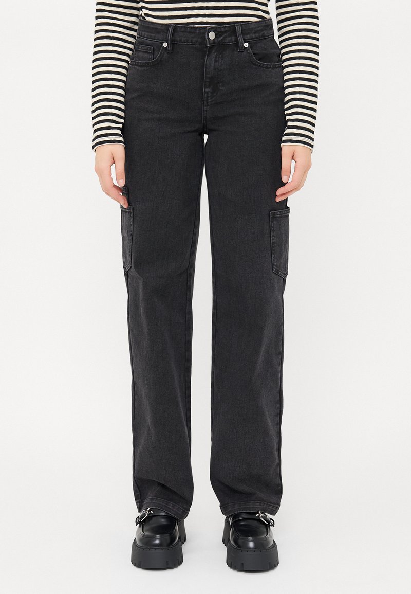 Pantaloni cargo in denim nero con vestibilità ampia, dotati di tasche laterali e una texture semplice. Abbinati a scarpe platform nere chunky.