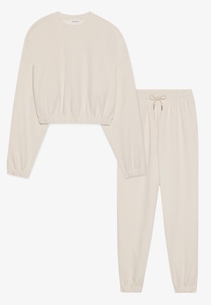 Set di abbigliamento da casa color crema composto da un top corto a maniche lunghe con orlo elasticizzato e pantaloni abbinati con vita elasticizzata e coulisse.
