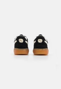 Sneakers in suede nero con dettagli bianchi, suole in gomma naturale e un accento dorato del logo sul tallone. Presentano un collare e una linguetta imbottiti.