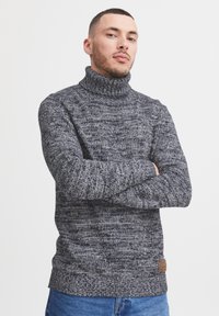 Dunkelgrauer Rollkragenpullover aus verschiedenen Strickstrukturen, mit einem gerippten Kragen und Saum sowie einem kleinen Lederlogo-Patch an der Seite.