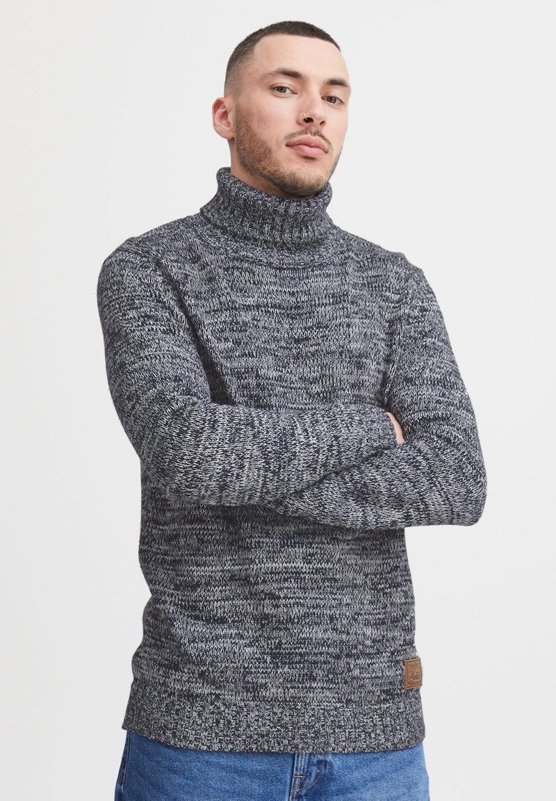Dunkelgrauer Rollkragenpullover aus verschiedenen Strickstrukturen, mit einem gerippten Kragen und Saum sowie einem kleinen Lederlogo-Patch an der Seite.