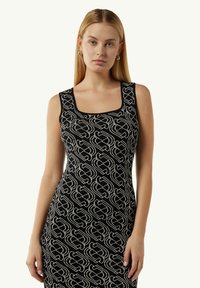 Schwarzes Tankkleid mit quadratischem Ausschnitt, das ein sich wiederholendes abstraktes Muster in Weiß auf einem strukturierten Stoff aufweist. Glatte Passform, ärmelloses Design.