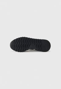 Semelle de chaussure avec une surface en caoutchouc noir texturé, présentant un motif ondulé et un détail de logo près de l'arche pour une meilleure adhérence.