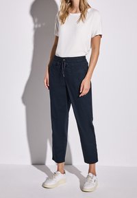 Granatowe spodnie na sznurek o luźnym kroju, zestawione z dopasowanym białym t-shirtem. Białe trampki z fakturowanym detalem na podeszwie.