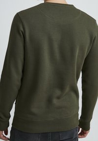 Sudadera verde oscuro con escote redondo, mangas largas y puños acanalados. Tejido suave que muestra una textura lisa y un detalle mínimo.