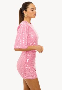 Robe rose recouverte de sequins, à manches courtes, au design cintré et à la surface texturée. Présentée sur un mannequin de profil.