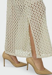 Falda midi de ganchillo en color beige con un patrón floral y una abertura lateral, combinada con zapatos de tacón nude. Textura detallada y tejido abierto.