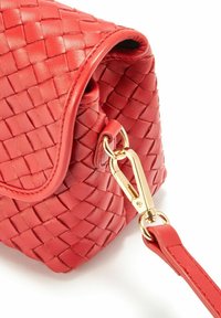 Czerwona torebka skórzana z plecionki z zaokrąglonym klapem, wyposażona w zamek w kolorze złotym oraz odpinany pasek. Tekstura jest gładka z wzorzystą powierzchnią.