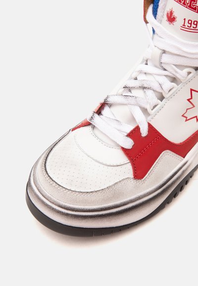 Gros plan d'une basket blanche avec une feuille d'érable rouge, des accents rouges, des lacets blancs et une semelle noire sur fond blanc.