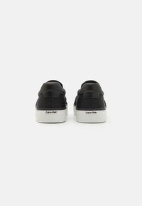 Svarte semsket sneakers med teksturert bakside, hvit gummisåle og subtil logo detalj på hælen. Strømlinjeformet, minimalistisk design.