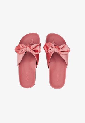 Par de sandalias tipo slide rosas de terciopelo con grandes lazos anudados en la parte superior, suela plana y diseño de punta abierta.