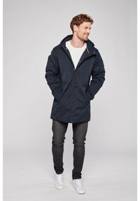 Námorní parka voděodolná s kapucí, předním zipem a dvěma bočními kapsami. V kombinaci s bílým svetr, tmavými džíny a bílými teniskami.