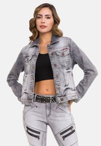 Grijze spijkerjack met een vervaagd ontwerp, knoopsluitingen en twee borstzakken. Gecombineerd met versleten grijze broek met ritsaccenten.