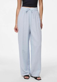 Svetlo modri široki hlače iz teksturirane tkanine, ki imajo elastičen pas z vrvico, nosijo pa se z črnimi sandali.