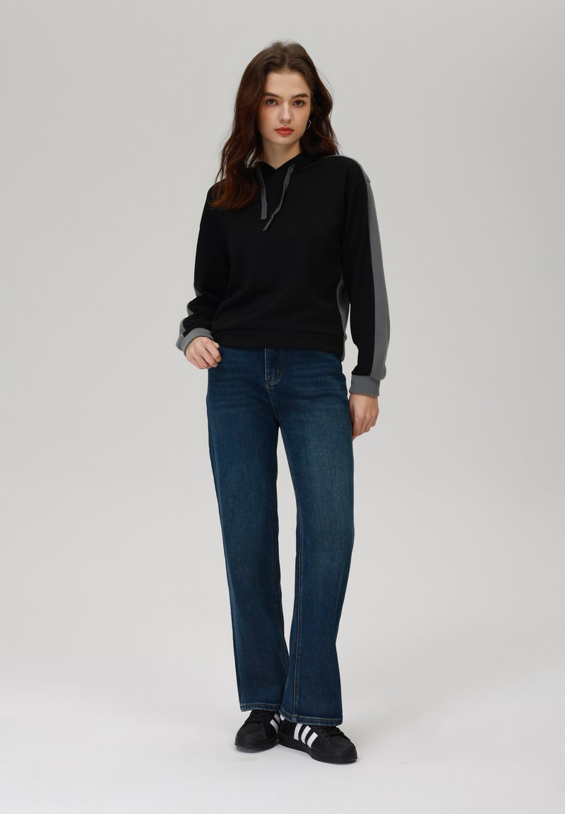 Czarna bluza z kapturem i szarymi rękawami, zestawiona z niebieskimi dżinsami o szerokich nogawkach oraz czarnymi trampkami z białymi paskami. Gładka tekstura tkaniny.