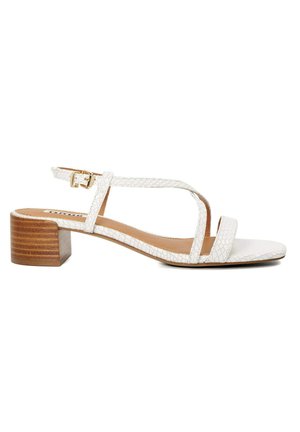 Sandale à talon blanche avec un dessus texturé, bout ouvert et un talon bloc. Dispose d'une bride de cheville avec un détail en boucle dorée.