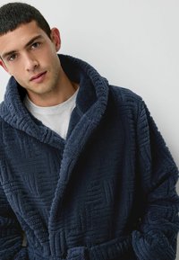 Granatowy szlafrok wykonany z fakturowanego polaru, z dużym kołnierzem szalowym, z delikatnymi wzorami geometrycznymi i paskiem do związania.