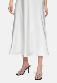 Sandales à talons ouverts noires avec des brides croisées ornées de strass, associées à une robe fluide en satin blanc.