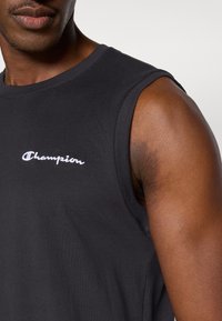 Μαύρο βαμβακερό αμάνικο μπλουζάκι με στρογγυλή λαιμόκοψη και κεντημένο λευκό λογότυπο "Champion" στο στήθος. Λείο ύφασμα και εφαρμοστό σχέδιο.
