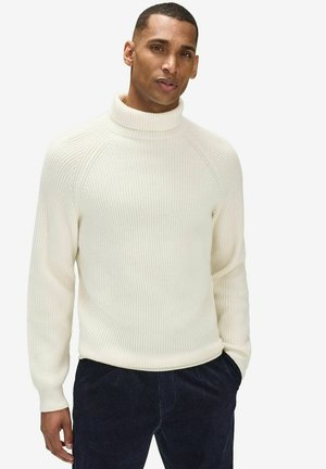 Kerman turtleneck neule, jossa on ribbitetty pinta ja raglan-hihat, yhdistettynä tummiin corduroy-housuihin. Puuvillasekoitemateriaali.