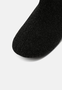 Black felt slipper with a rounded toe, textured surface, and no visible hardware. Simple design focuses on comfort and warmth.