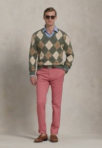 Kootud argyle-sviiter rohelises, beežis ja pruunis, helesinise särgi peal; kontrastsuseks roosad püksid ja pruunid libisevad kingad. Prillid peas.