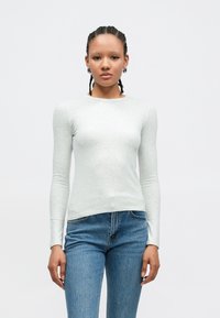 Ανοιχτό γκρι τοπ με μακριά μανίκια και στρογγυλή λαιμόκοψη, εφαρμοστό σχέδιο, κατασκευασμένο από απαλό ύφασμα, συνδυασμένο με μπλε τζιν παντελόνι ψηλόμεσο.