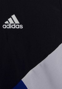 Svart tyg sportkläder med vitt Adidas-logotyp; har blå och vita geometriska detaljer. Texturerad yta, modern design, kontrasterande färger.