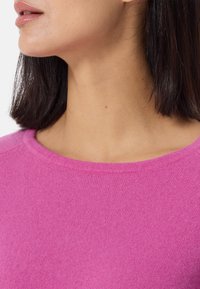 Maglione rosa con collo rotondo, realizzato in un tessuto a maglia liscio, caratterizzato da un design semplice e dettagli senza cuciture sulle spalle.