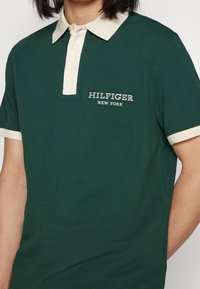 Zelené polo tričko s kontrastním krémovým límečkem a manžetami, na hrudi s vyšívaným logem "HILFIGER NEW YORK".
