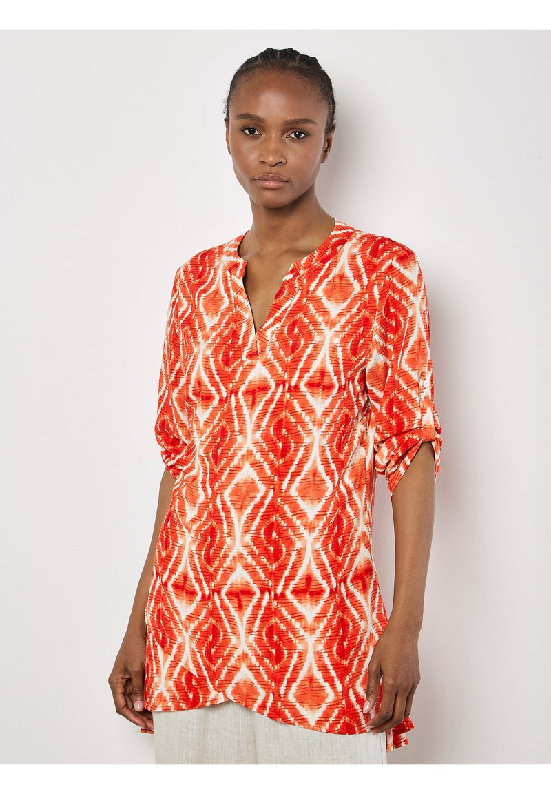 Rot-weiße gemusterte Tunika mit V-Ausschnitt, kurzen Ärmeln und einem etwas längeren Rückenteil, aus leichtem Stoff gefertigt.