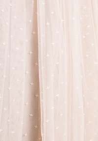 Tissu beige transparent doux avec de petits motifs en relief en forme de points et une texture fine en résille, drapé en plis délicats.