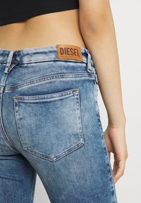 Närbild av en person som bär blå Diesel-jeans och en svart kort cropped topp, där bakfickan och det lädermärkta märket syns.