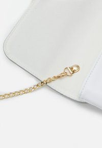 Bílá peněženka s hladkým povrchem, zlatým řetízkovým popruhem a zacvakávacím uzávěrem. Interiér má jemnou látkovou podšívku.