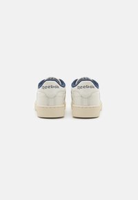 Hvite lær sneakers med marineblå semsket skinn detaljer ved hælen, med en teksturert kremgummisåle og Reebok-merke.