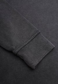 Tumma harmaa collegekangas, jossa on teksturoitu pinta, varustettuna hihansuun resorilla ja saumattomilla ompeluyksityiskohdilla kestävyydelle.