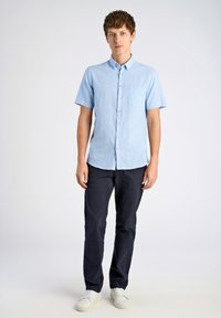 Korte mouwen, lichtblauw gestreept shirt met knoopsluiting en borstzak, gecombineerd met marineblauwe broek en witte sneakers. Soepele stoftextuur.