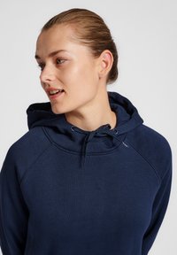 Granatowa bluza z kapturem, z regulowanym sznurkiem, o miękkiej fakturze i rękawach raglanowych. Projekt zawiera minimalistyczne logo na piersi.