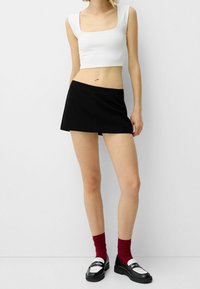 Svart kort kjol med en vit kortärmad topp. Toppens har en fyrkantig halsringning; kjolen har en enkel och ren design. Svarta skor och röda strumpor.